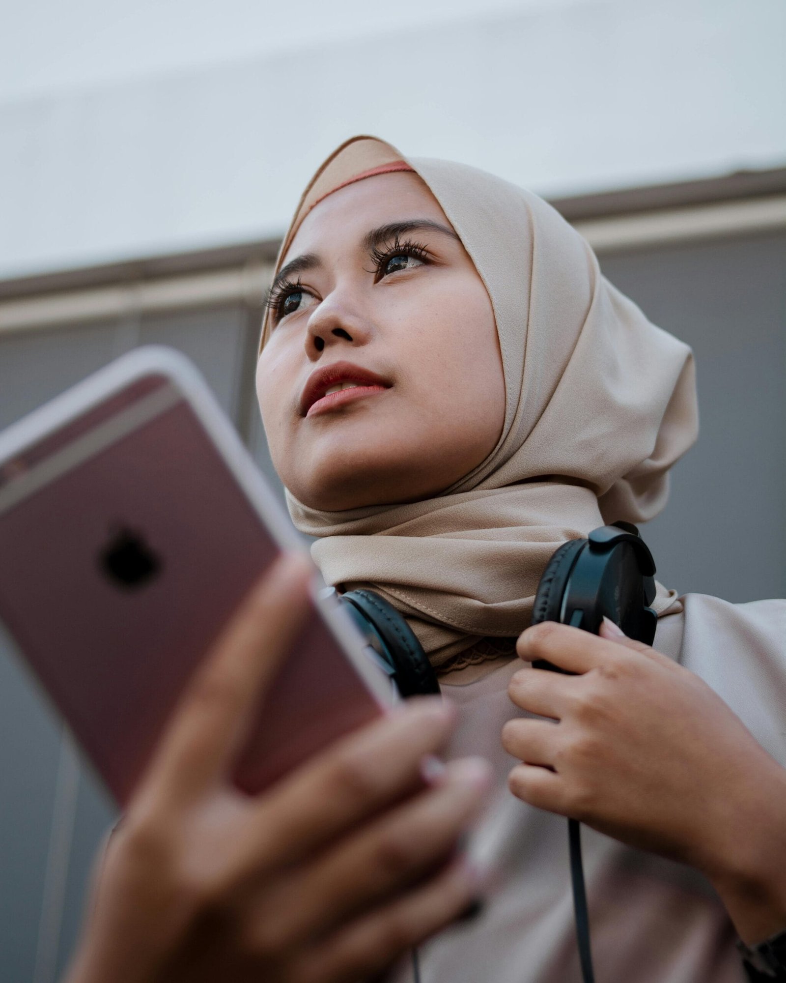 Young woman in hijab using smartphone and headphones, embodying contemporary tech lifestyle.